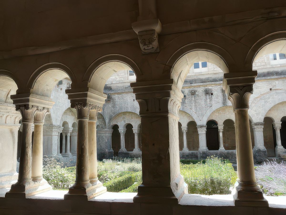 Travée de la galerie est du cloître, montrant trois arcades reposant sur des colonnes géminées (jumelles). Remarquez la tête de démon, la Tarasque, et qui fait face au Père abbé assis dans la salle du chapitre.