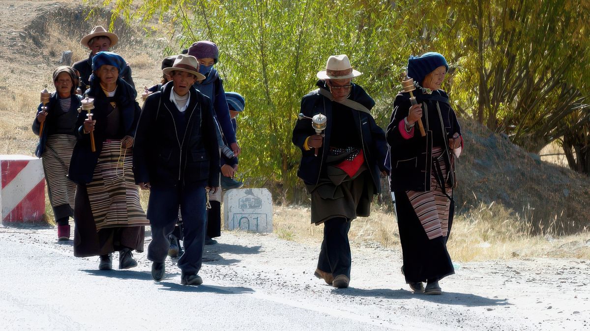 Ces pèlerins sont des Khampas; en plus du ruban rouge, les hommes portent un chapeau qui ressemble à celui des cowboys. Ce sont des nomades de la région du Kham (ancienne région du Tibet). Normalement les femmes ont aussi de jolies coiffures ornées de pierres mais elles ont un foulard sur la tête pour les protéger du soleil et du vent.