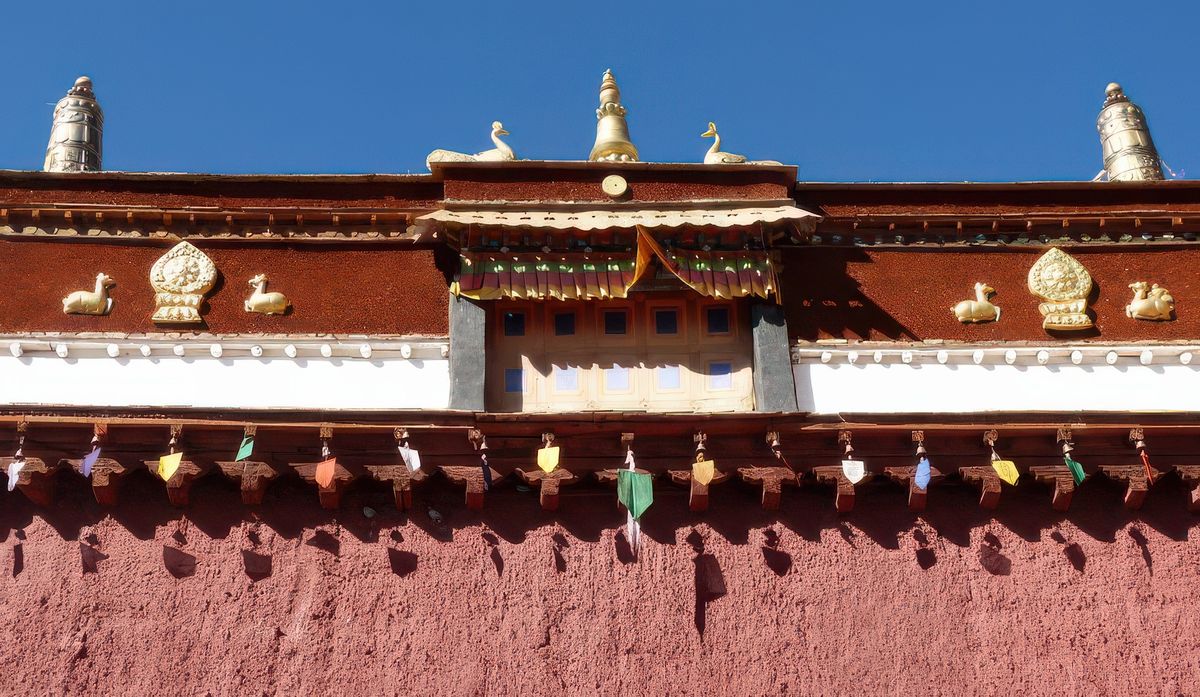 Différents symboles religieux: tout en haut, de chaque côté, deux dhvajas (cylindres dorés), en dessous, au milieu, un pignon d'or entouré par deux oiseaux (des paons), en dessous de chaque côté, deux daims entourant la roue du Dharma. Des drapeaux de prières sont accrochés à des petites cloches tibétaines qui tintent joliment.