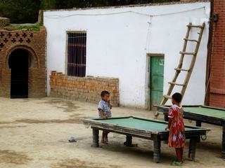Les jeux de billard sont présents partout en Chine. Dans les villes, mais aussi dans de nombreuses maisons, même isolées dans les campagnes, et bien sûr dans les rues ... Sans doute comme peut l’être le baby foot pour les petits capverdiens.
Sur ce cliché, pris dans la région de Turfan au nord ouest de la Chine, ces enfants turbulents se sont vu confisquer par leur maman les cannes du billard, ce qui ne les empêche pas de bien se marrer, et de nous proposer leur version de « jeux interdits » .
Le jeux de billard s'adresse à tous, petits et grands, comme le montre ces deux tables d'une hauteur différente.