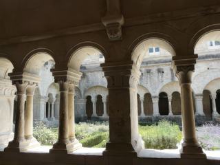 Travée de la galerie est du cloître, montrant trois arcades reposant sur des colonnes géminées (jumelles). Remarquez la tête de démon, la Tarasque, et qui fait face au Père abbé assis dans la salle du chapitre.