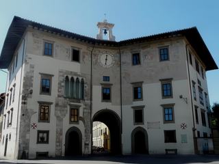 Le palazzo dell'Orologio (palais de l'Horloge) a été édifié en 1605-1608 par l'union de l'ancien palais médiéval du capitaine du peuple et de la Torre della Fame, où mourut le comte Ugolino de la Gherardesca, un épisode raconté par Dante dans sa Divine Comédie. La réunion des deux éléments se voit encore dans la façade incurvée de l'ensemble et la voûte centrale, qui divise l'édifice en deux. Il est décoré de fresques réalisées au XVIIe siècle par Vasari. Bien que très dégradées, une partie de ces fresques sont encore visibles dans le tiers supérieur de l'édifice. Jusqu'en 1804, il servit de résidence aux vieux chevaliers de l'ordre de Saint Etienne. Depuis le début du XXe. siècle, il fait office de bibliothèque de la Scuola Normale Superiore.