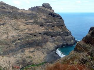 Les terrasses dégringolent sur les flancs des falaises volcaniques qui tombent dans l'océan. Tout en bas, on aperçoit le lit d'une petite rivière.