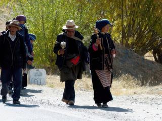 Ces pèlerins sont des Khampas; en plus du ruban rouge, les hommes portent un chapeau qui ressemble à celui des cowboys. Ce sont des nomades de la région du Kham (ancienne région du Tibet). Normalement les femmes ont aussi de jolies coiffures ornées de pierres mais elles ont un foulard sur la tête pour les protéger du soleil et du vent.