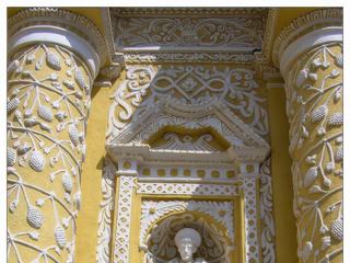 La façade stuquée de blanc sur fond jaune est décorée d'une profusion exubérante de motifs, surtout des grappes de raisin.