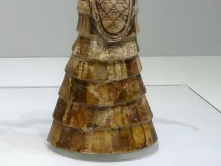 Avec sa robe élégante et riche qui lui découvre une poitrine généreuse pour symboliser sa fertilité, cette déesse aux serpents est magnifique. Elle porte un félin sur son chapeau, et des serpents lui enserrent les bras et elle en tient un dans chaque main. Le serpent qui rampe sous les pierres et qui hiberne sous des souches ou dans des trous sous la terre est considéré comme un animal chthonien en relation avec le monde infernal, la déesse domine donc toute la nature, sous et sur la terre avec le serpent et le félin.