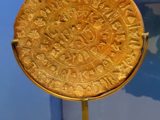 Trouvé sur le site de Phaestos, ce disque a un diamètre de 16 cm et présente des inscriptions sur les deux faces. Il a été retrouvé par l’Italien Pemier en 1908. Ces inscriptions creusées dans l’argile, à l’aide de sceaux, dans un sillon en colimaçon composé de soixante-et-un segments, restent un véritable mystère. Il daterait de 1600-1450 avant JC. L’écriture hiéroglyphique est totalement inconnue à à ce jour, elle ne se retrouve nulle part ailleurs. Une évidence archéologique fait attester qu’il s’agisse d’une pièce cultuelle puisque retrouvée dans la partie réservée au culte sur le site de Phaestos, dans une niche où il y avait du charbon, des os d’animaux .